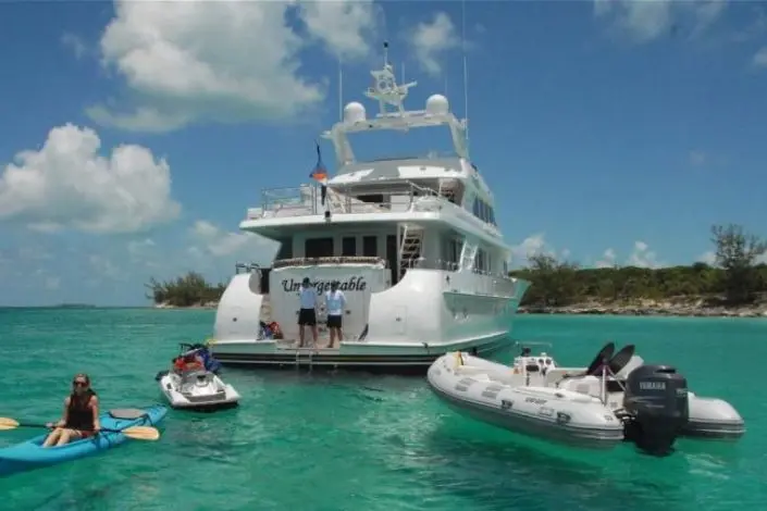 Crewed motor yacht at anchor in turquoise water with tenders alongside
