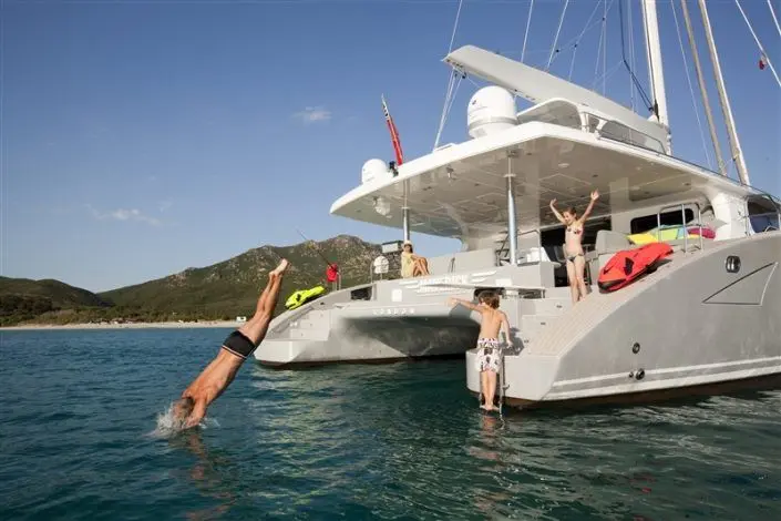 Guests diving from the stern of a crewed catamaran at anchor