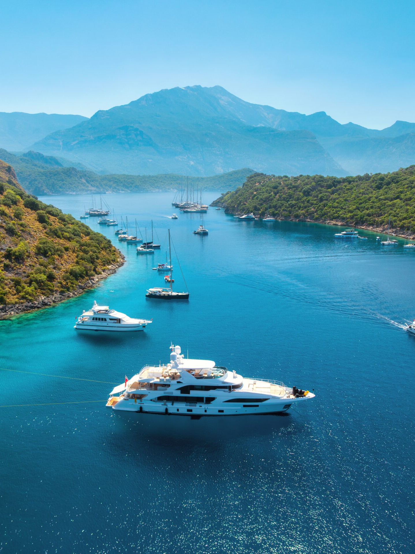 Aerial view of a motor yacht anchored in a sheltered bay with the fleet behind her
