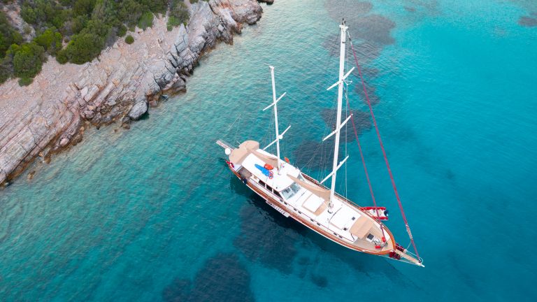 A sailing gulet at anchor in turquoise water, seen from above