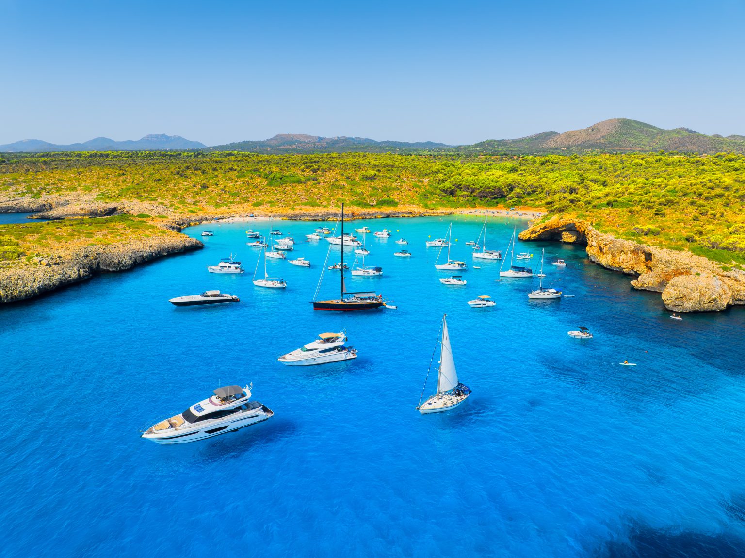 Yachts anchored in a turquoise bay on the coast of Mallorca, seen from the air