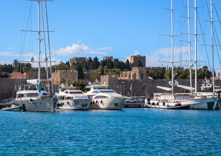 Yachts moored in Mandraki Harbour below the medieval walls of Rhodes Old Town, in the Dodecanese